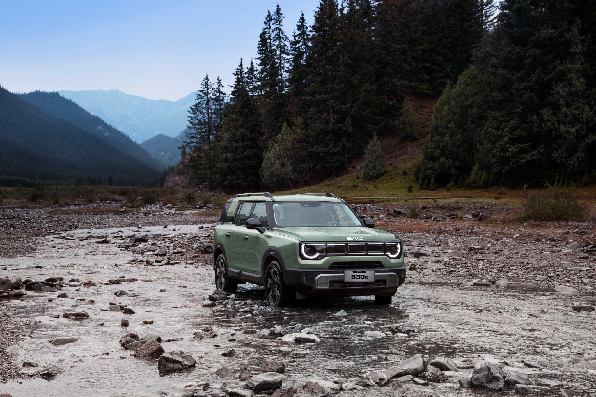 BAIC B30e driving through a rocky river bed in a forested valley